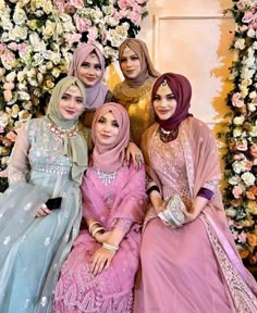 four women in hijabs posing for a photo together with flowers behind them and one woman wearing a headscarf