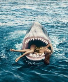 a woman laying on top of a shark in the ocean with it's mouth open