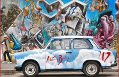 an old blue car parked in front of a graffiti wall