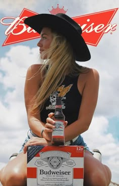 a woman sitting on top of a box with a beer bottle in her hand and a budweiser sign above her head