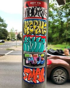 a pole with some graffiti on it next to a street and parked cars in the background