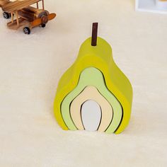 a wooden toy with a green pear on the top and an airplane in the background