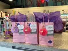 three pink shopping bags with pom - poms are sitting on a counter in a store