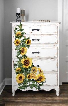 a white dresser with sunflowers painted on the top and bottom, sitting in a room