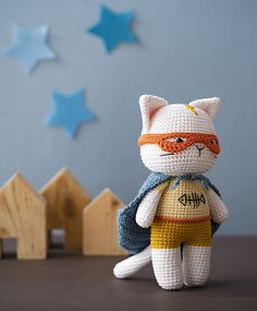 a crocheted white cat with a red mask and blue cape is sitting on a table