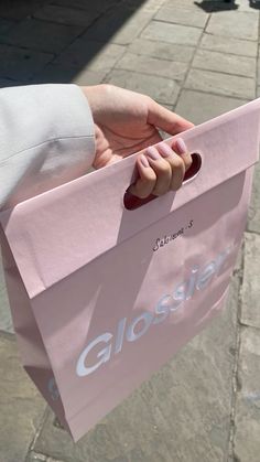 a person holding a pink shopping bag with the word glossier on it's side