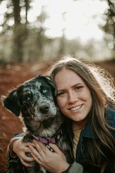 a woman is holding her dog in the woods