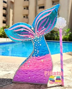 a colorful mermaid tail sculpture next to a swimming pool with a pink and blue umbrella