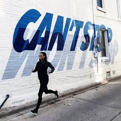 a woman running down the street in front of a wall that says can't stop