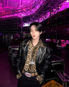 a woman wearing a leopard print shirt and black leather jacket standing in front of a stage