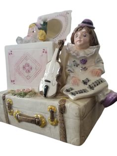 a figurine sitting on top of a suitcase with a violin and other items