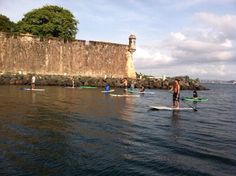 a group of people on surfboards in the water near a stone wall and lighthouse