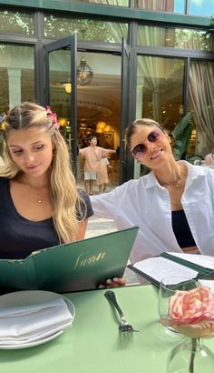 two beautiful women sitting at a table in front of an open menu book and papers