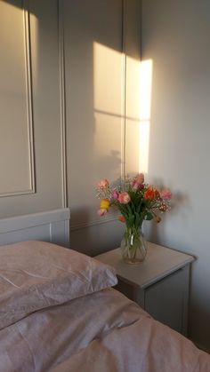 a vase filled with flowers sitting on top of a white table next to a bed