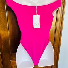 a pink and white one piece swimsuit hanging on a wooden door with a price tag attached to it