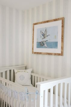 a baby's room with striped wallpaper and white crib bedding, framed art above the crib