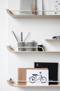 two wooden shelves with books, cups and other items on them in a white room