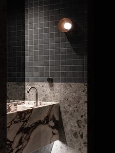 a bathroom sink sitting under a light next to a tiled wall