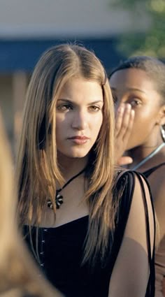 two beautiful young women standing next to each other in front of a crowd with one looking at the camera