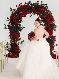 a woman in a wedding dress standing next to a floral arch with roses on it