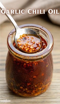 a jar filled with chili sauce on top of a wooden table next to a spoon