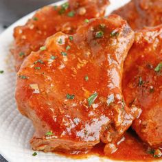 two pieces of meat covered in marinara sauce on a white plate with parsley