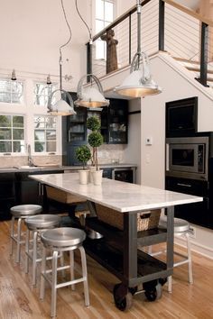 a kitchen island with stools and lights hanging from it's ceiling, in front of an open floor plan