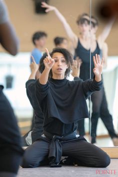 a woman sitting on the floor with her hands in the air while others are doing yoga