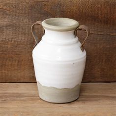 a white ceramic vase sitting on top of a wooden table next to a wood wall