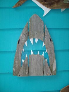 a wooden shark mask hanging on the side of a blue building with two birds perched on it