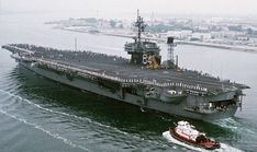 an aircraft carrier being towed by a tug boat