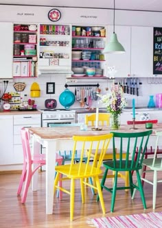 the kitchen table is painted bright colors and has colorful chairs in front of it, along with white cabinets