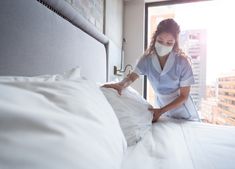 a woman wearing a face mask while sitting on a bed in front of a window