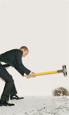 a man in black suit holding a large hammer over a metal ball with one hand