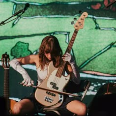 a woman sitting on top of a chair while holding a bass in front of her