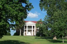 a large white house sitting on top of a lush green field next to tall trees