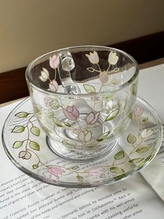 a glass cup and saucer sitting on top of an open book with flowers painted on it