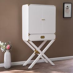 a white cabinet sitting on top of a wooden stand next to a vase with flowers