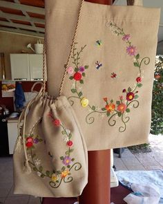 two bags with embroidered flowers on them hanging from a wooden pole in front of a kitchen