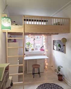 a loft bed with a desk underneath and stairs to the upper level, in front of a window