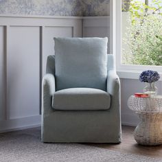 a blue chair sitting in front of a window next to a table with a vase on it