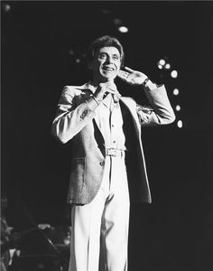 a man in a suit and tie standing on stage with his hands to his ears