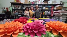 three women standing in front of a table with paper flowers on it and other crafting supplies behind them