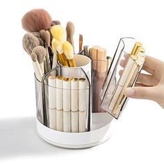 a person holding a cup filled with lots of makeup brushes and other cosmetics in it