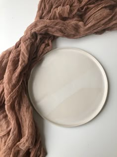 a white plate sitting on top of a table next to a brown scarf