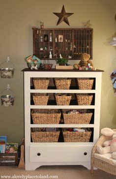 a white dresser with baskets on top of it next to a teddy bear and other toys