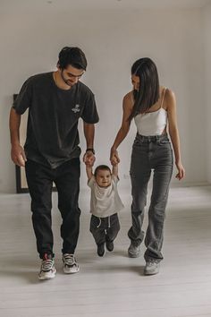 a man, woman and child walking in an empty room with white walls holding hands