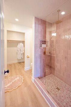 a bathroom with pink tiled walls and wooden flooring next to a walk in shower