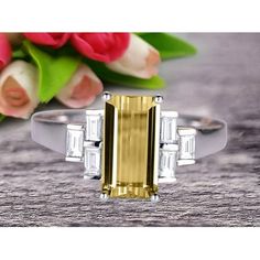 a yellow and white diamond ring sitting on top of a wooden table next to flowers