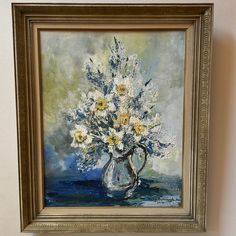 a painting of white and yellow flowers in a silver vase on a wall above a shelf